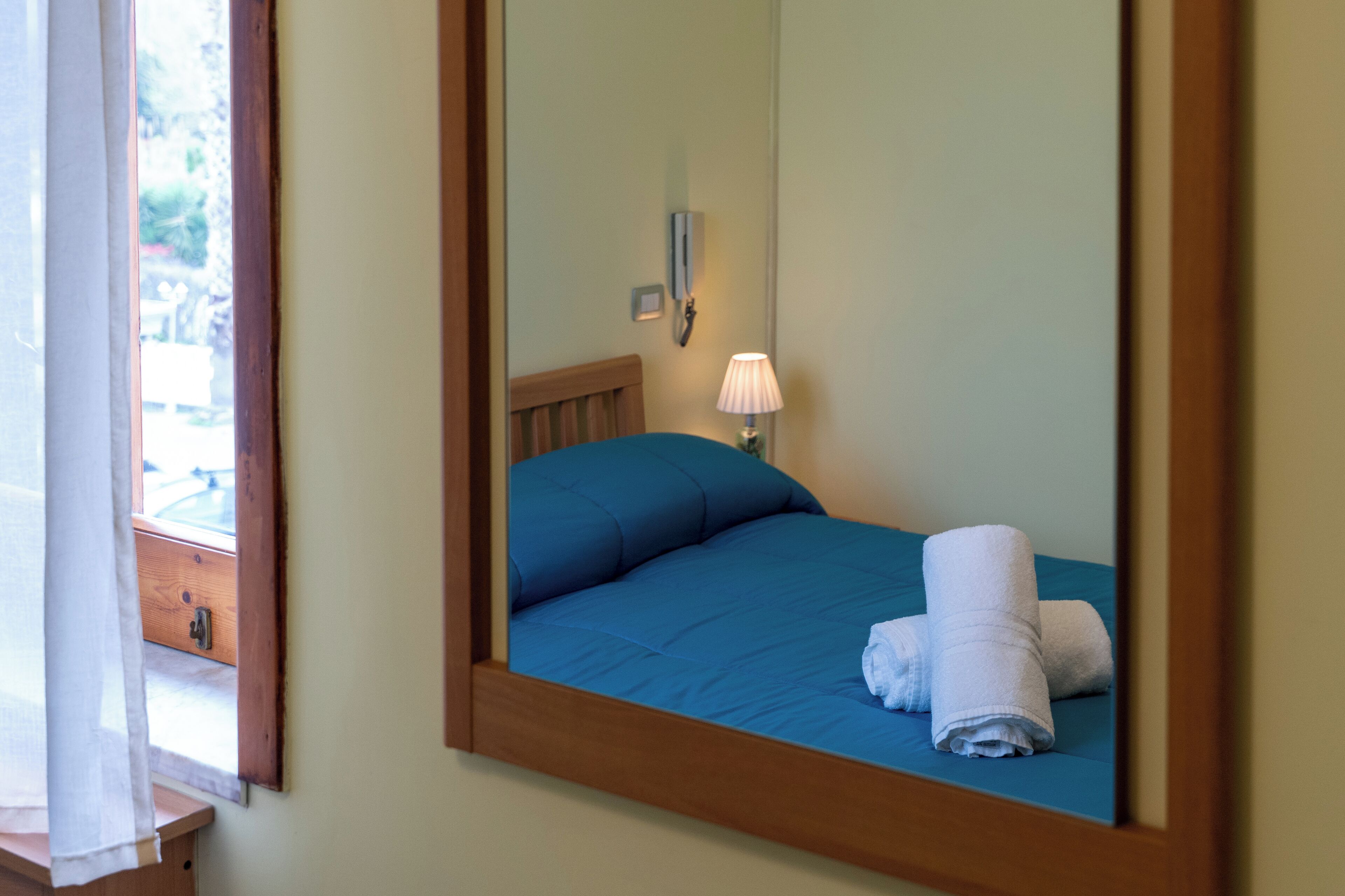 Una habitación de hotel con una cama, una mesita de noche, una lámpara y una ventana con cortinas.