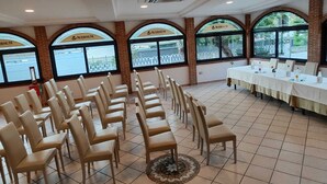 Ein Konferenzraum mit mehreren Reihen beiger Stühle, einem langen Tisch mit weißem Tuch und großen Fenstern, auf denen der Name "AVERNUM" zu sehen ist.