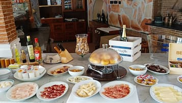 Una mesa de buffet con diversos alimentos, incluyendo carnes, quesos y una estación de queso fundido.
