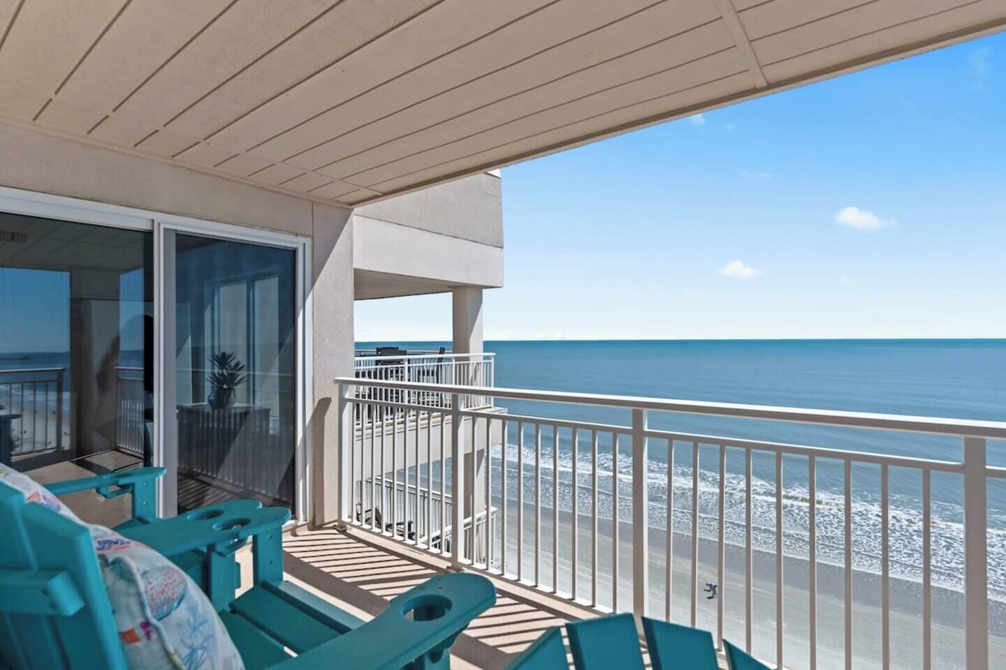 A balcony with a view of the ocean, a sliding glass door, and outdoor seating.