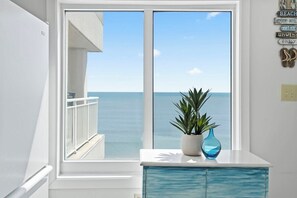 A room with a large window overlooking the sea, a white cabinet, and a potted plant. - Corner, Oceanfront Balcony- Pool- Upscale Design (North Myrtle Beach)