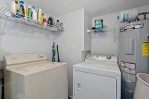 Un cuarto de lavandería con dos lavadoras, un estante con artículos de limpieza y un calentador de agua.