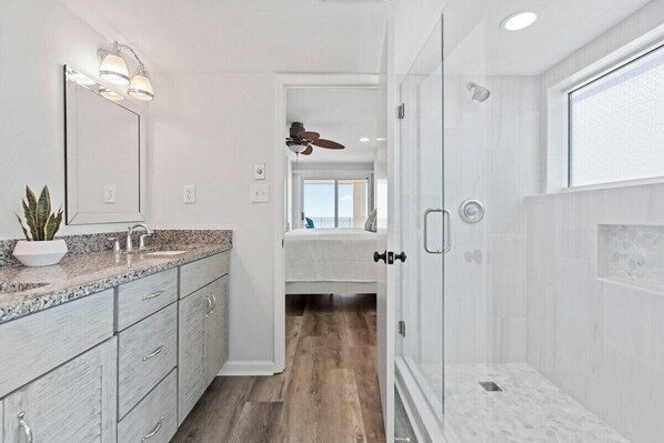 A modern bathroom with a large mirror, granite countertop, and a walk-in shower.