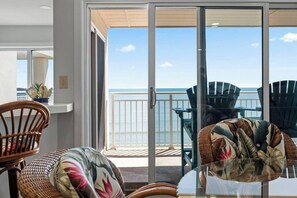 A room with a view of the sea, a glass door leading outside, and outdoor seating with chairs.