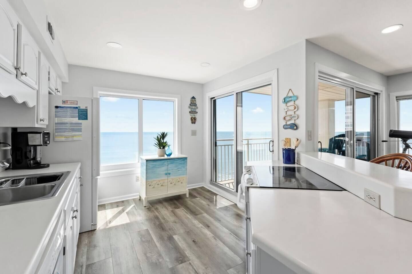 A modern kitchen with a view of the sea, a dining area with a view, and a balcony with a railing.