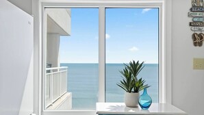 A room with a large window overlooking the sea, a white cabinet, and a potted plant. - Corner, Oceanfront Balcony- Pool- Upscale Design (North Myrtle Beach)