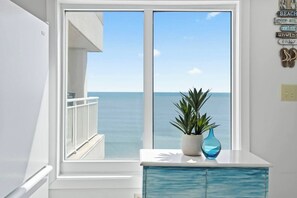 Een kamer met een groot raam met uitzicht op zee, een wit kastje en een bloempot.