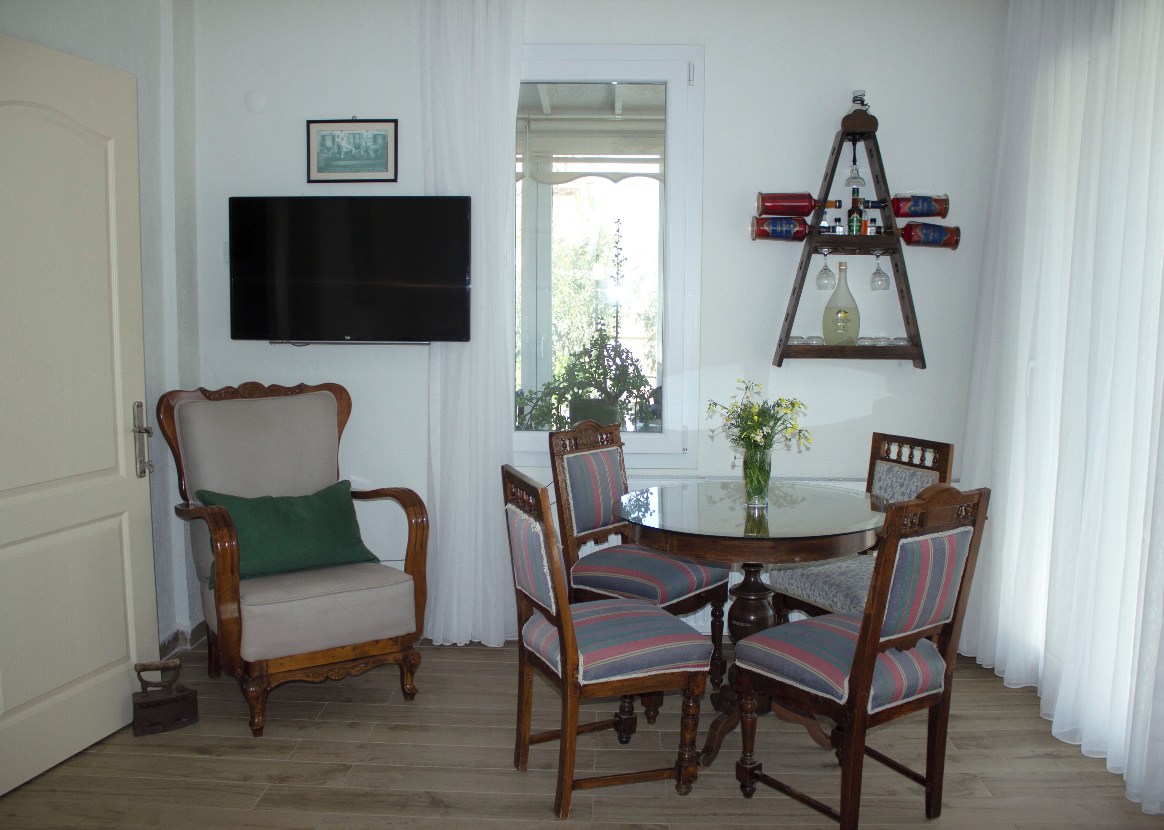 A dining area with a round table, four chairs, a television mounted on the wall, and a ladder with bottles.