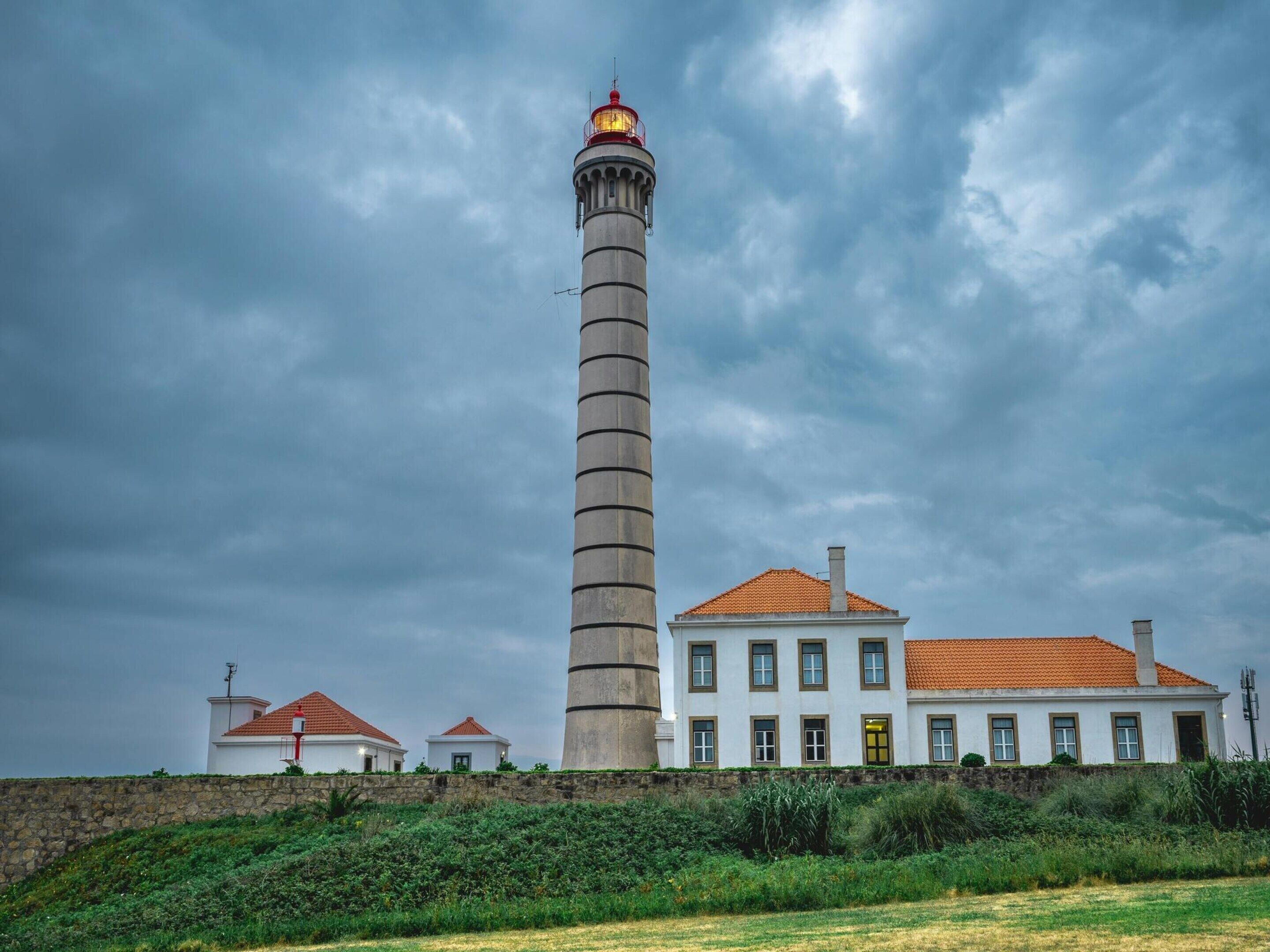 A lighthouse with a tall, cylindrical tower and a red top, adjacent to a white building with a red-tiled roof.