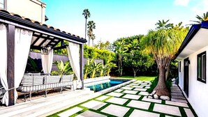 A pool area with a geometric tile pattern, a pergola with white curtains, and lush greenery.