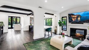 A modern living room with a fireplace, a television, and a dining area with a view of the outdoors.