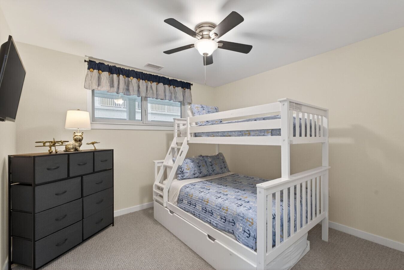 A bunk bed with a ceiling fan, a dresser with drawers, and a window with curtains.