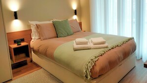 Een net opgemaakt bed met een groen en roze dekbedovertrek, twee bedlampjes en een nachtkastje met een groene kaars.