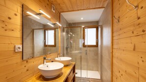 Ein modernes Badezimmer mit Holzwänden, zwei Waschbecken, einer Duschkabine aus Glas und einem großen Spiegel.