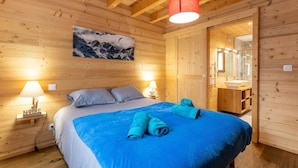 Ein Zimmer in einer Holzhütte mit einem Bett, zwei Nachttischlampen, einem Bergpanorama und einem durchgegangenen Tür erkennbaren Badezimmer.