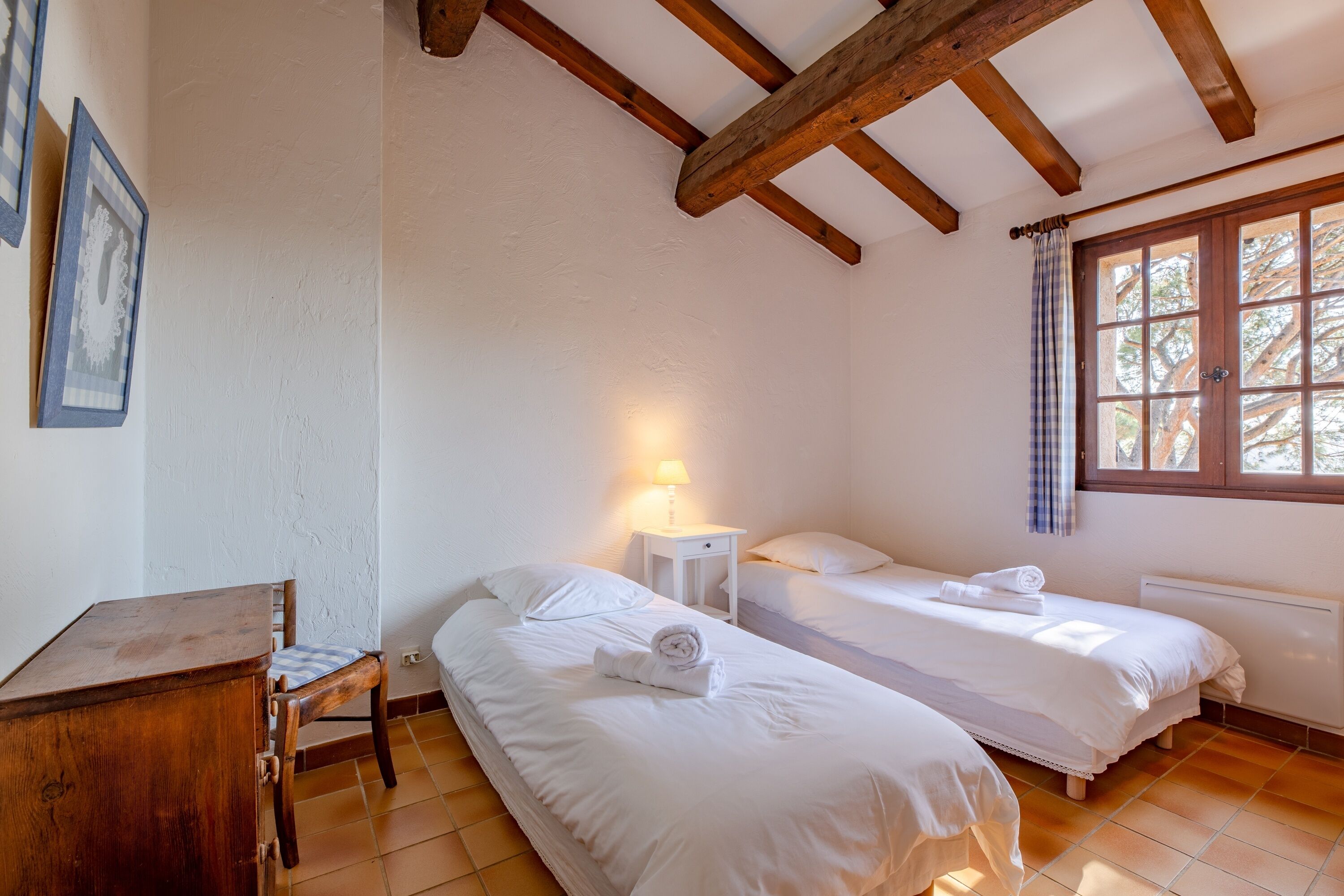 Une chambre avec deux lits, un bureau en bois et une fenêtre avec des rideaux.