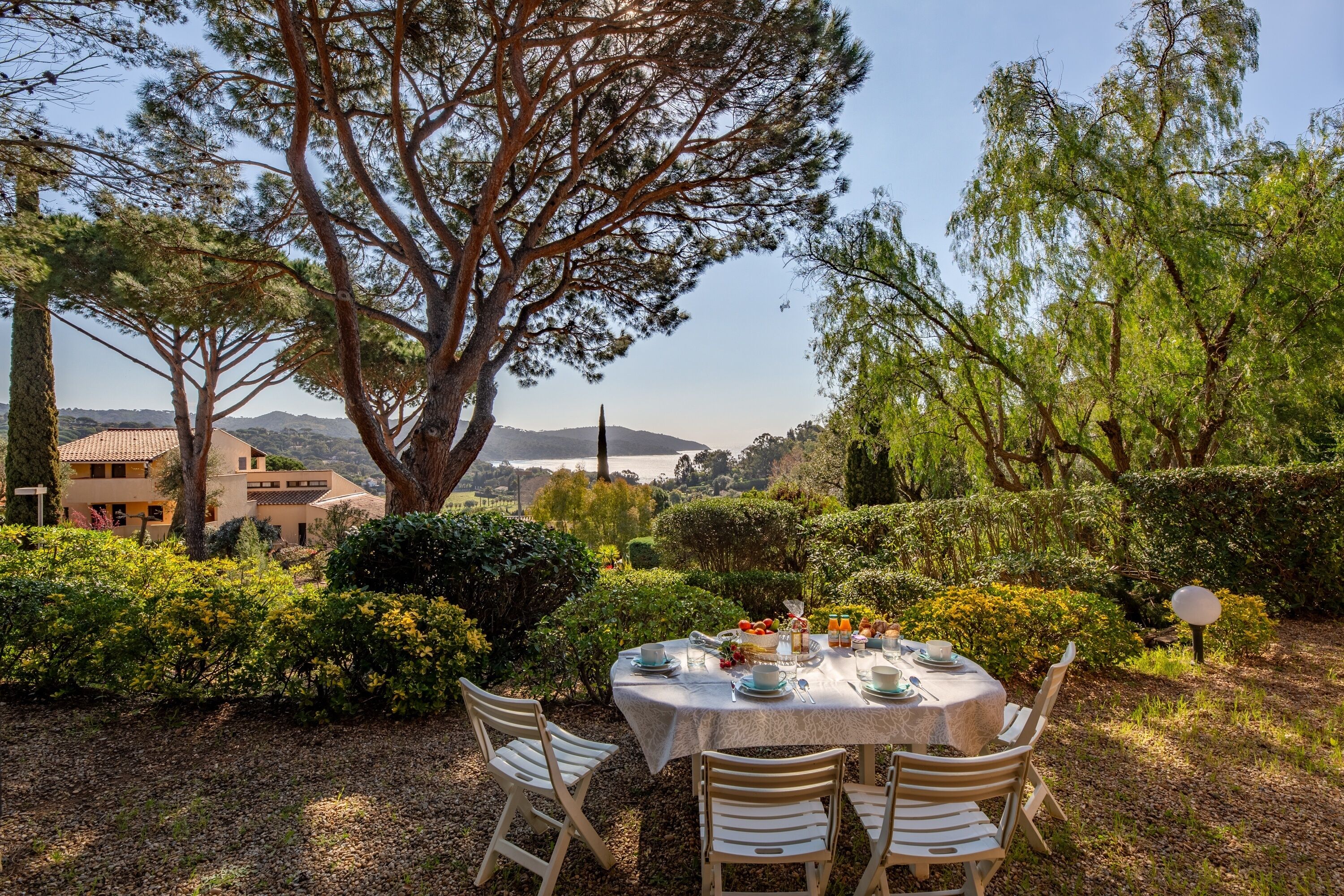 An outdoor dining area with a table set for four, surrounded by lush greenery and a view of distant hills.