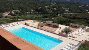 Ein Pool auf dem Dach mit Liegestühlen, umgeben von Grünflächen und Hügeln im Hintergrund.