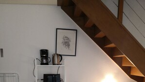 A dining area with a round table covered by a patterned tablecloth, surrounded by white chairs. A coffee maker and a kettle are on a shelf above the table. A framed picture hangs on the wall, and a lamp provides light in the corner. - Three semi-detached houses downtown Grenoble (Grenoble)