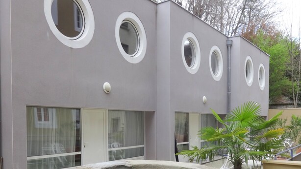 A building with circular windows and a large stone planter in the foreground. - Three semi-detached houses downtown Grenoble (Grenoble)