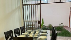 Een eetgedeelte met een glazen tafel en houten stoelen, omringd door een decoratief metalen hek en een kleine tuin.