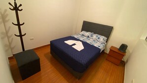 Een slaapkamer met een bed, een kapstok, een klein houten kistje en een zwarte poef.