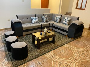 Een hoekbank met bijpassende fauteuils, een salontafel en een kamerbreed tapijt in een goed verlichte kamer met betegelde vloer.