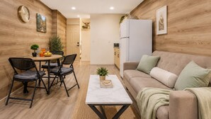 Un espacio habitable compacto con comedor, sofá, mesa de centro y zona de cocina.