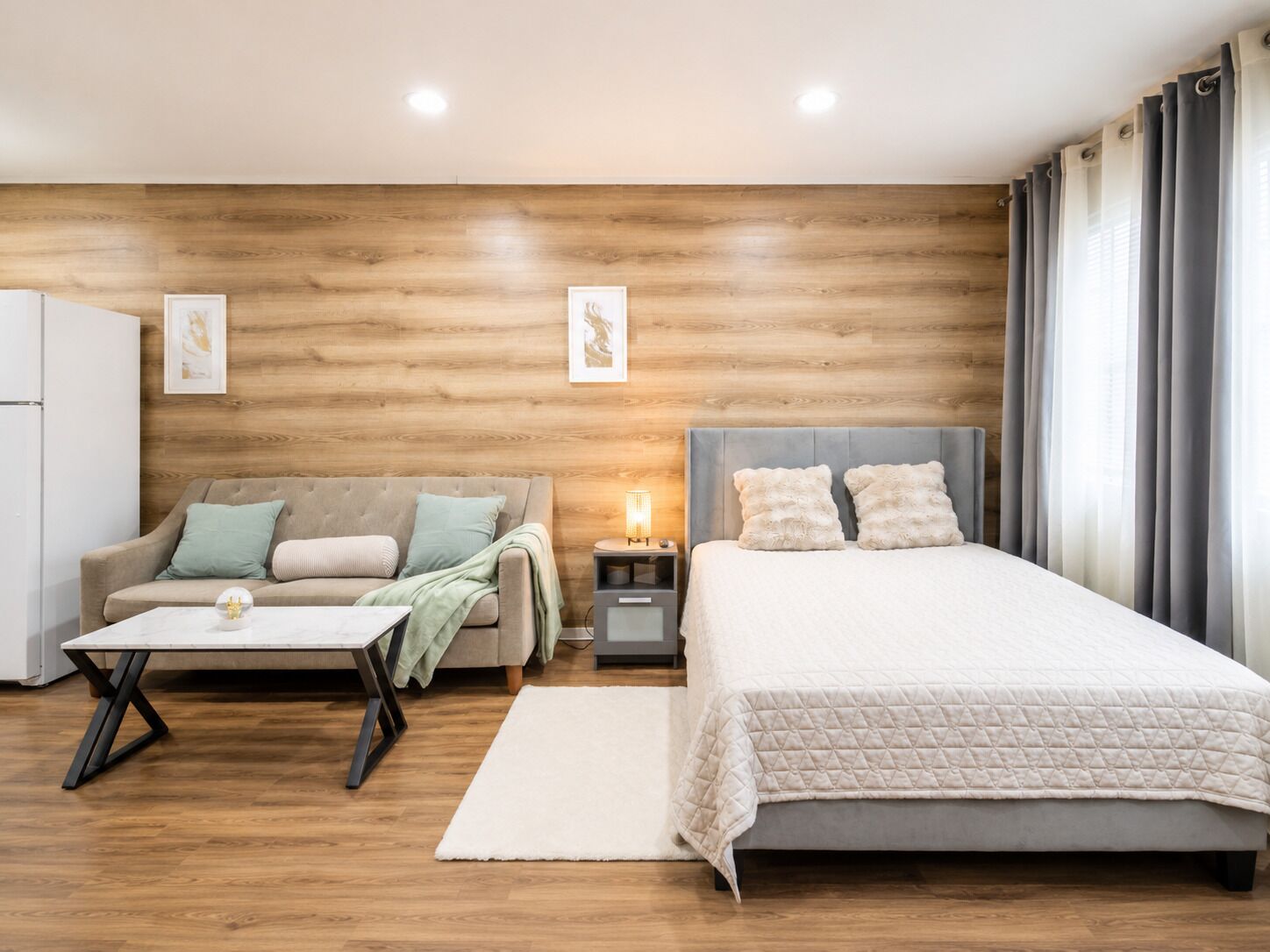 Ein modernes Schlafzimmer mit einer Holzwand, einem Bett, einem Schlafsofa, einem Nachttisch und einem kleinen Tisch.