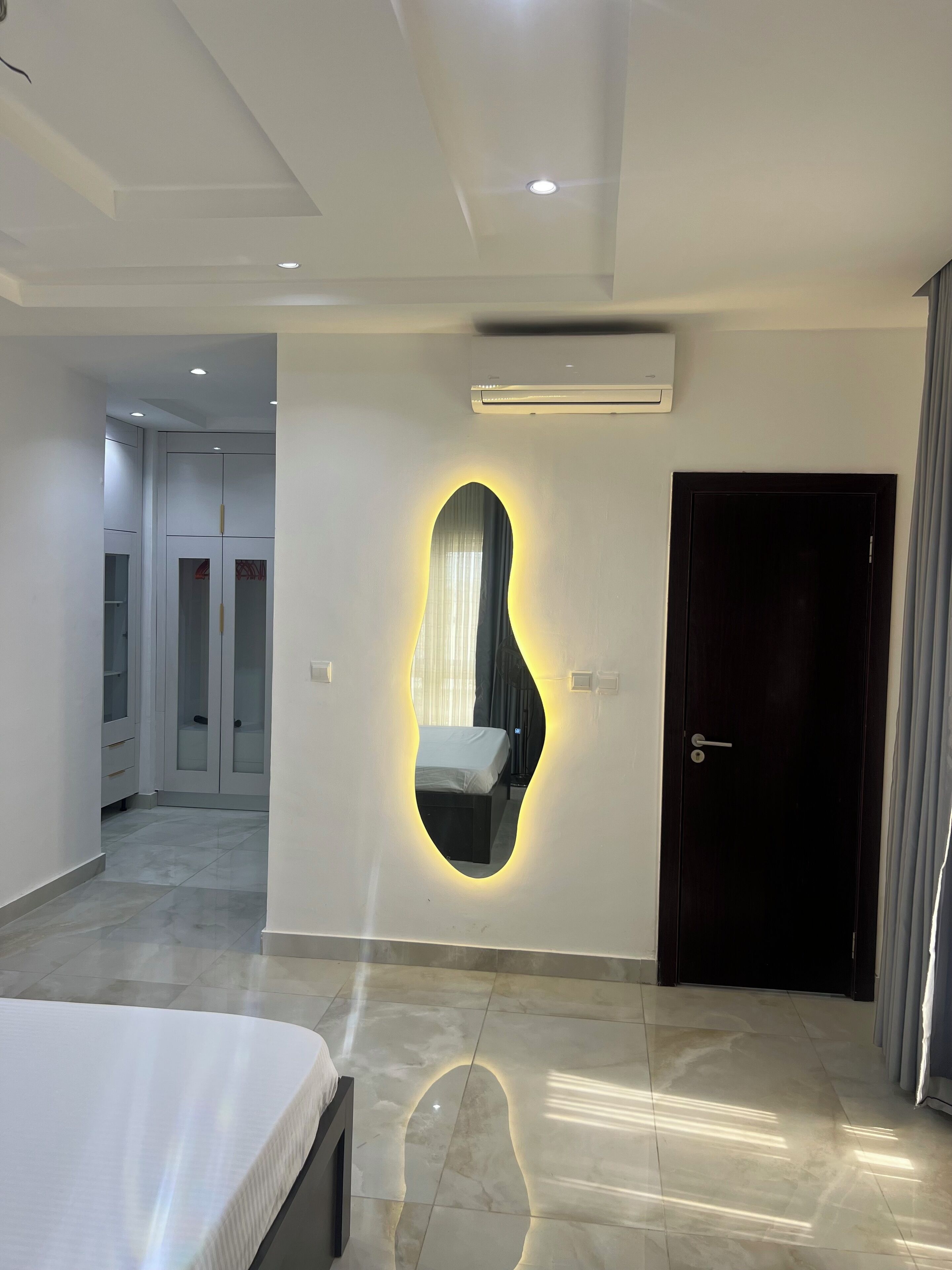 Une chambre à coucher moderne avec un lit, un miroir fixé au mur et une porte.