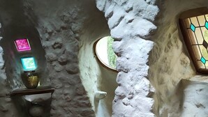 A rustic stone interior with a round wooden table, a small shelf with a neon sign, and a stained glass window. - Ker-terre de Flo - 2 pers (STE COLOMBE)