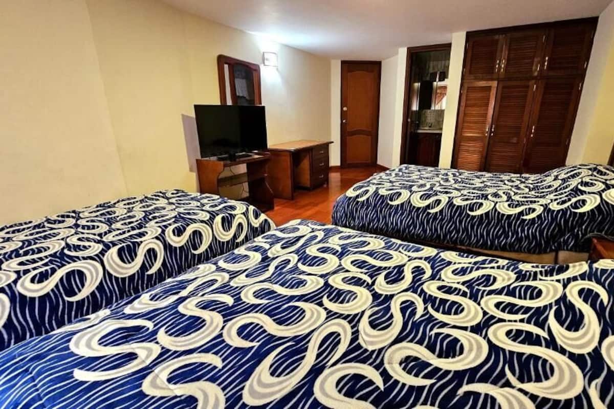 Ein Hotelzimmer mit zwei Betten, einem Schreibtisch, einem Fernseher und einem Kleiderschrank.