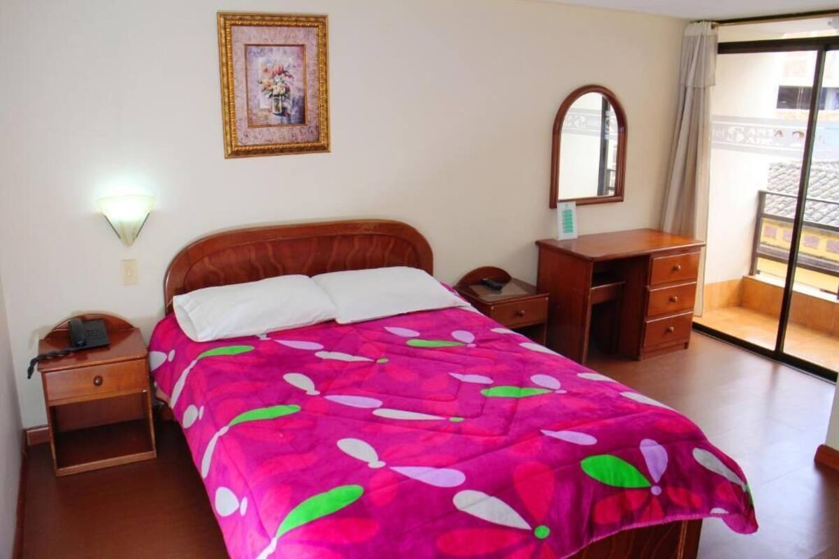 Ein Schlafzimmer mit Bett, Nachttisch, Kommode, Spiegel und Blick auf einen Balkon.
