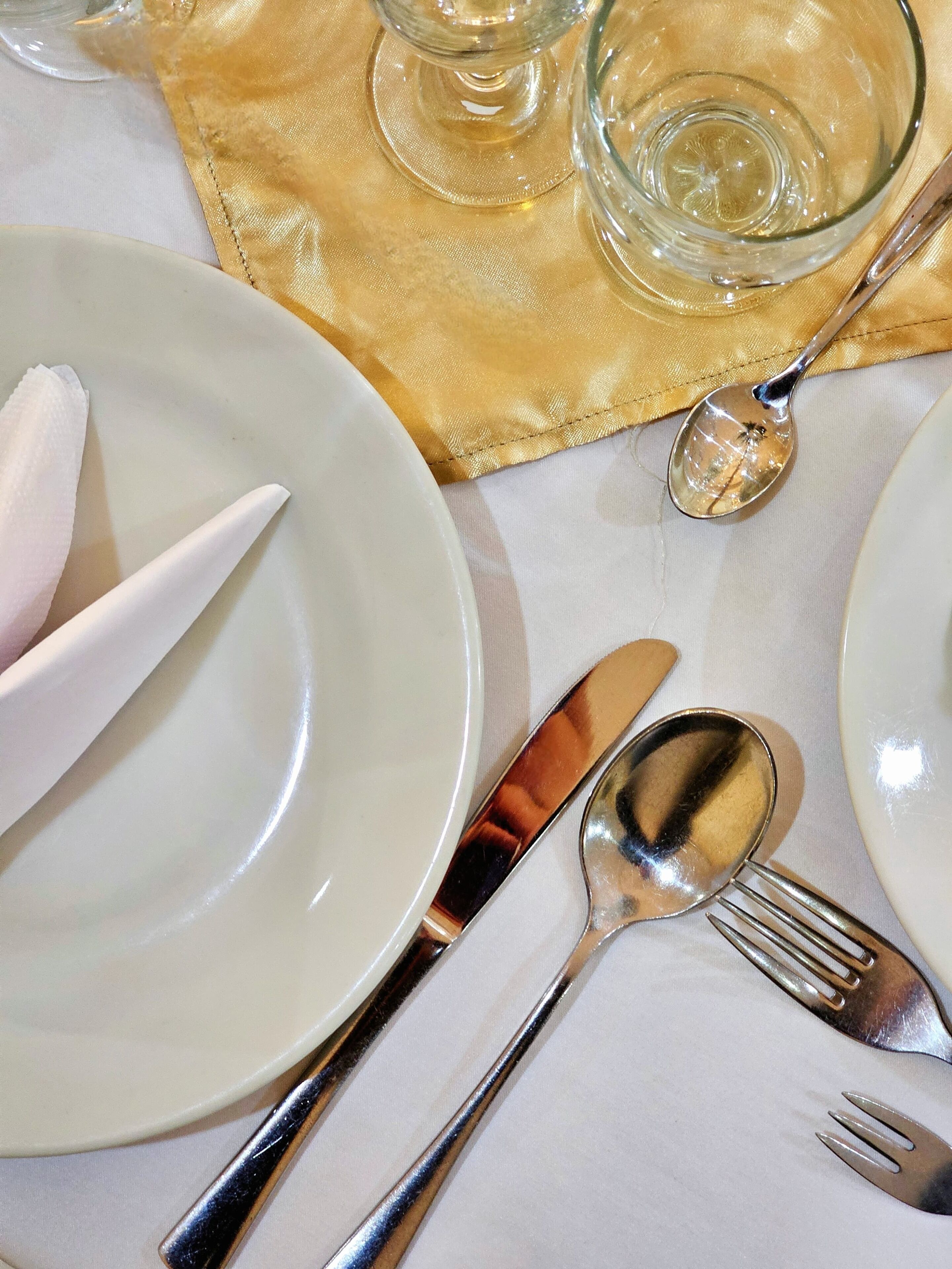 Una mesa dispuesta con platos blancos, cubiertos y una servilleta dorada.