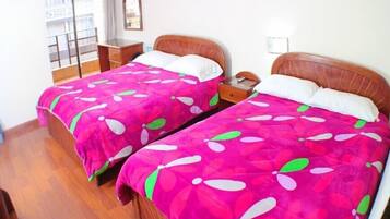 Two beds with matching pink floral bedding, wooden headboards, and a small bedside table with a phone.