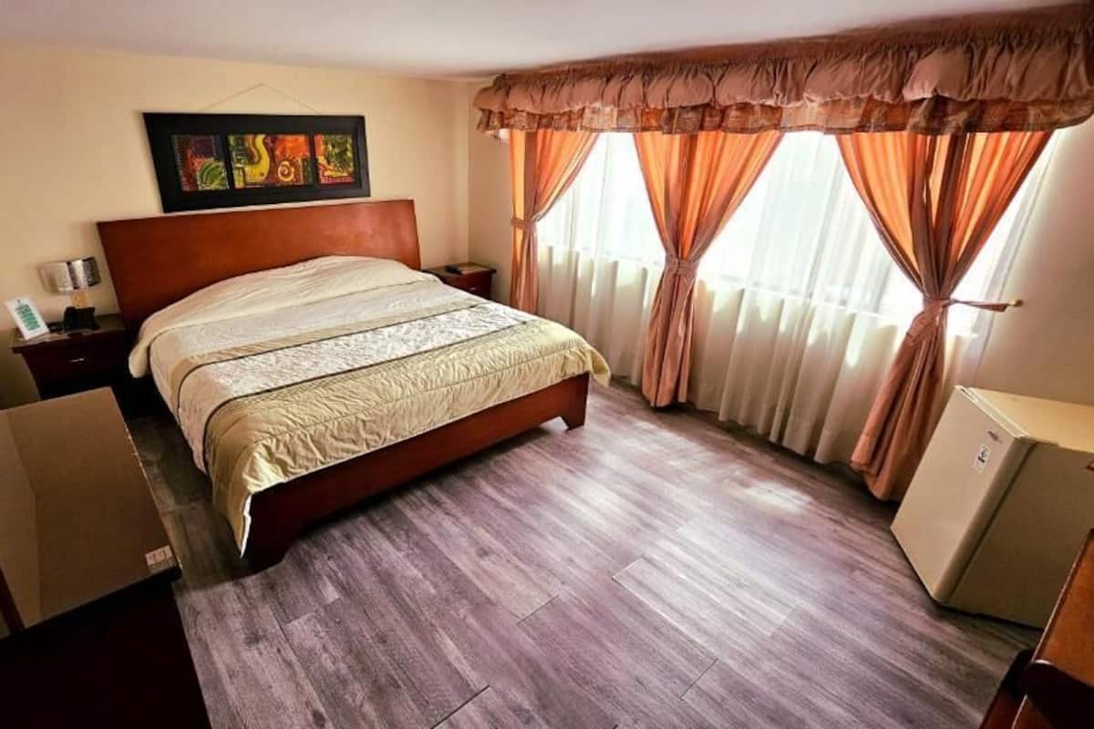 Ein Hotelzimmer mit einem großen Bett, einem Nachttisch, einem Schreibtisch und einem Schrank.