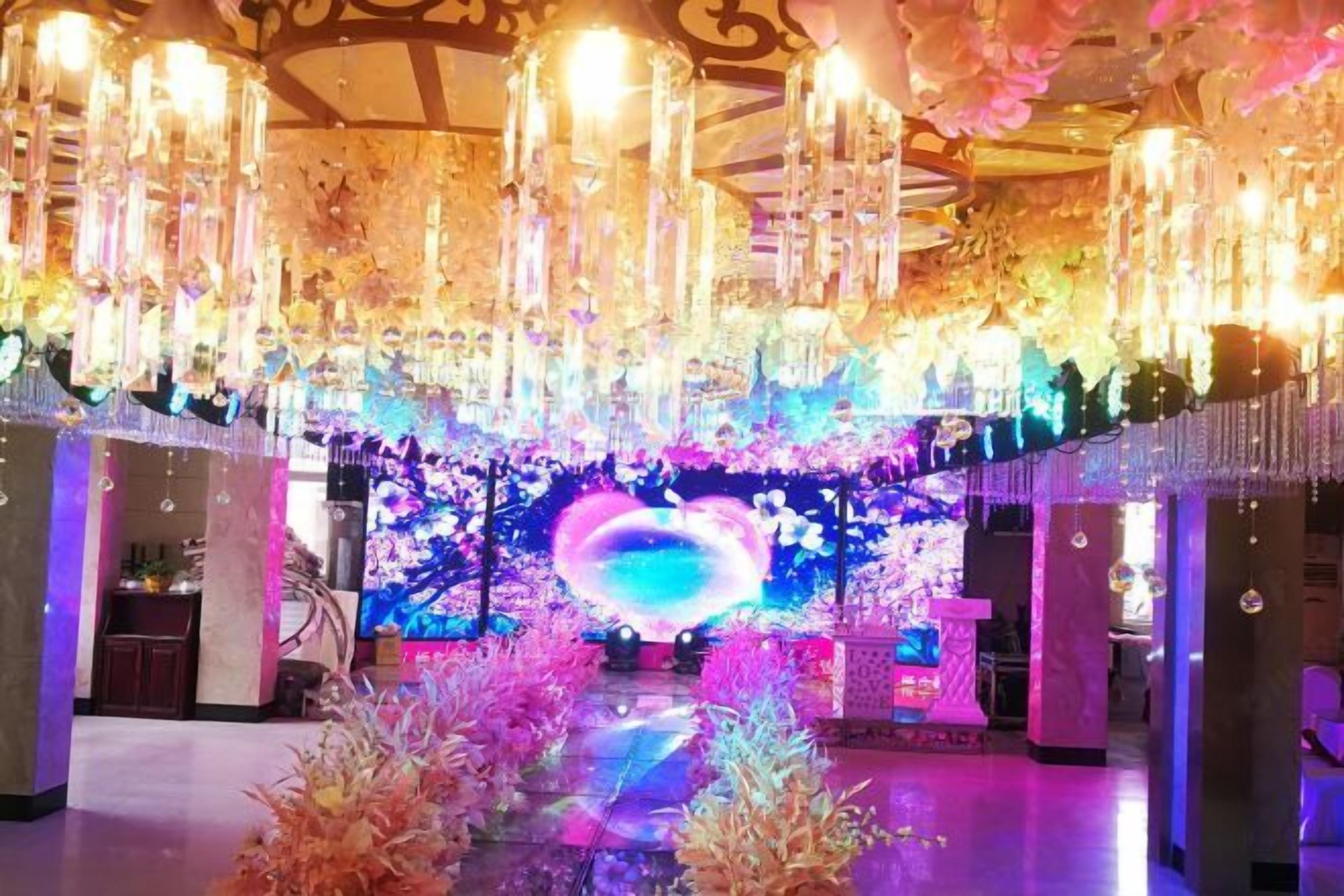 Un intérieur luxueux agrémenté de lustres, une scène dotée d’un grand écran et des décorations florales.