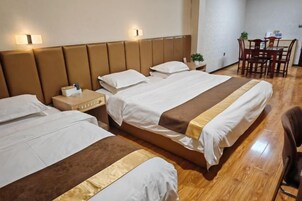Habitación de hotel con dos camas, piso de madera, una mesa de comedor con sillas y una planta pequeña en la mesita de noche.
