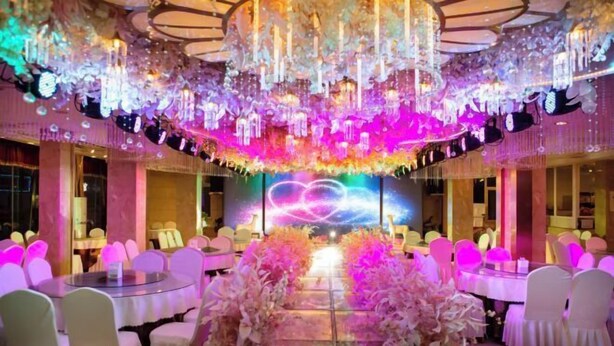Une salle de banquet avec des tables rondes, des chaises blanches et une composition florale centrale.