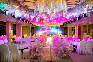 Un salón de banquetes con mesas redondas, sillas blancas y un arreglo floral central.