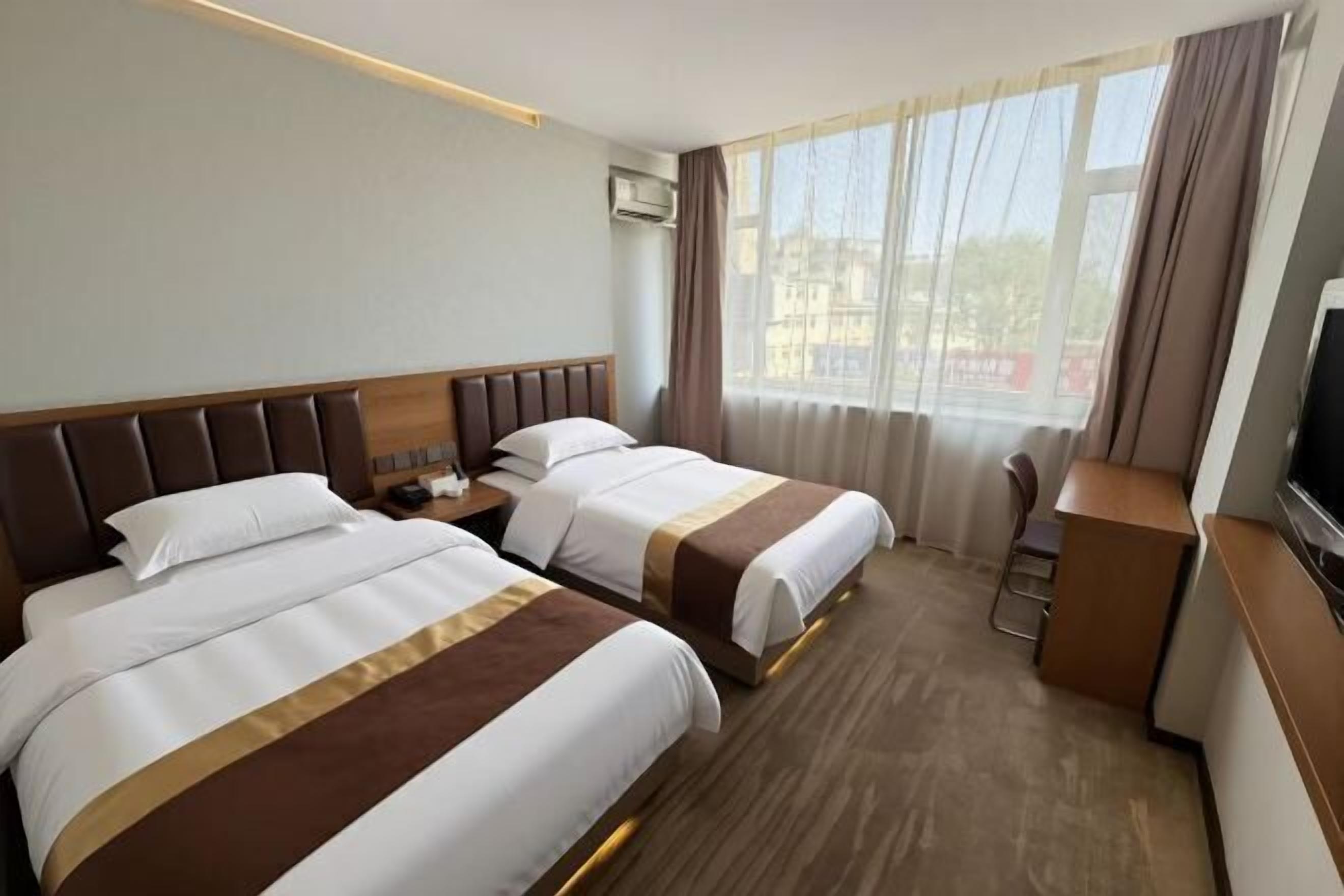 A hotel room with two beds, a desk, a TV, and a window with curtains.
