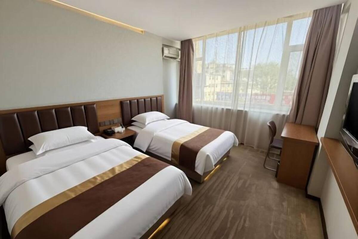 Een hotelkamer met twee bedden, een bureau, een televisie en een raam met gordijnen.