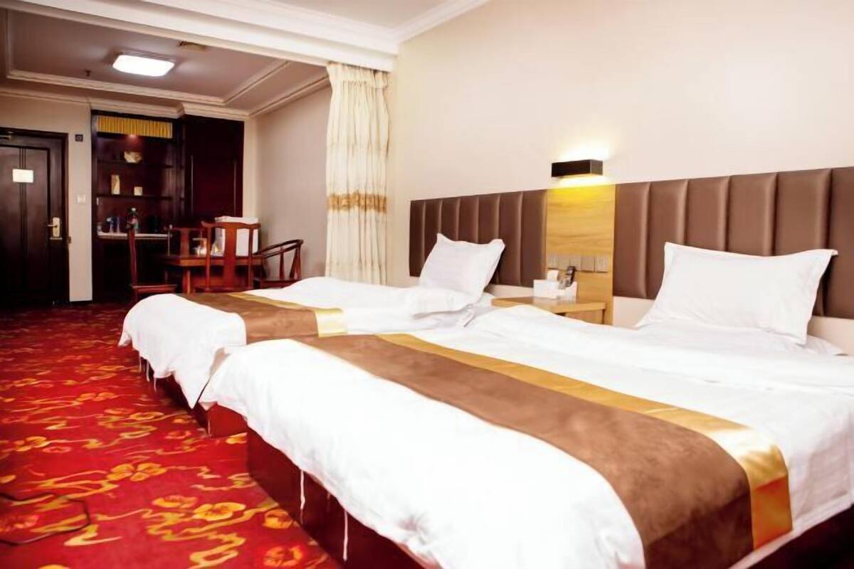 Een hotelkamer met twee bedden, een rood tapijt, een houten stoel, een bureau en een nachtkastje.