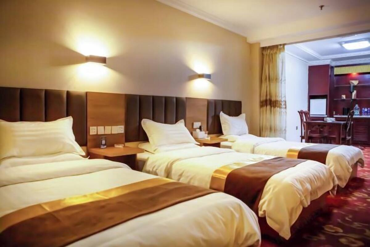 Een hotelkamer met drie bedden, een bureau en een stoel.