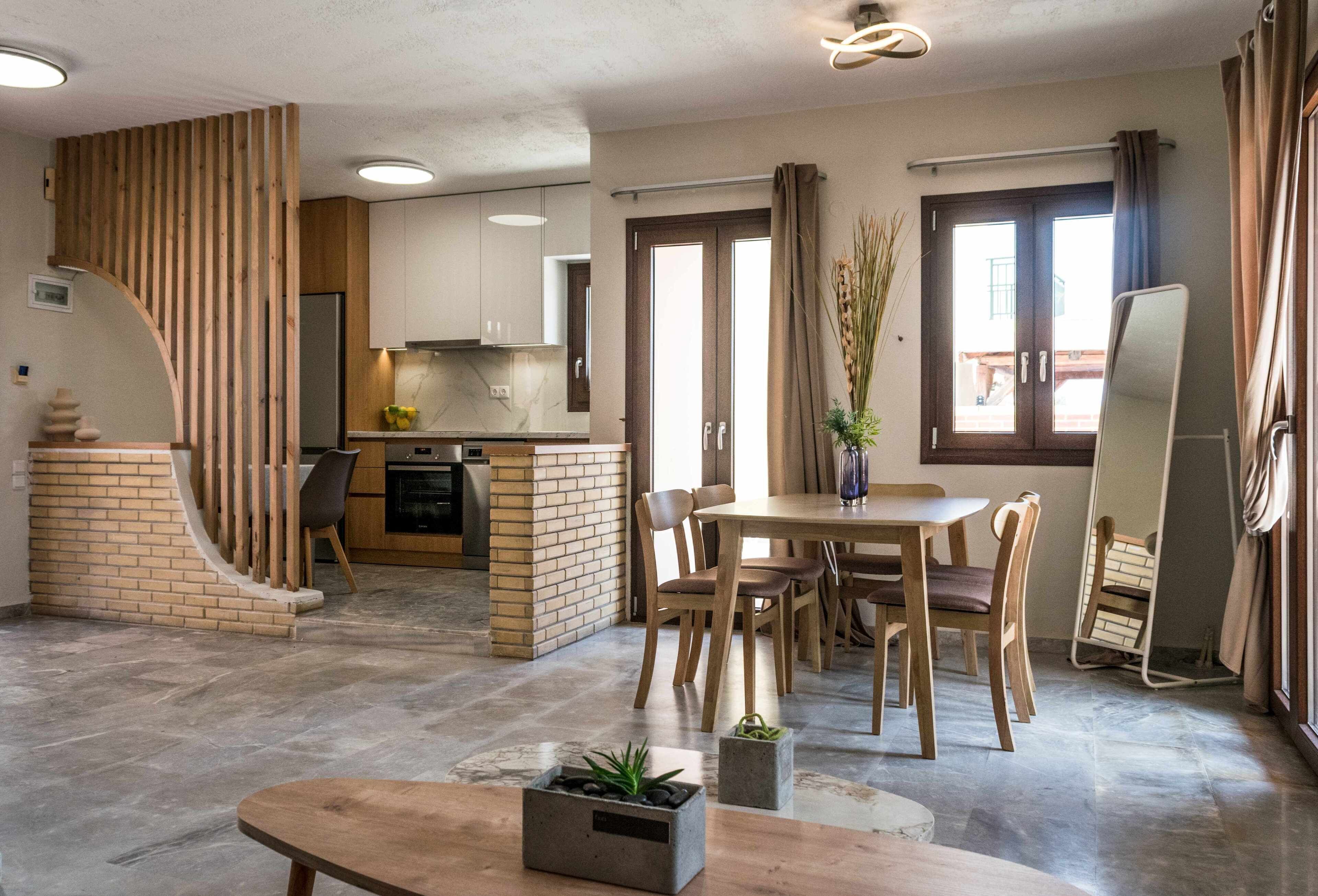 Een moderne keuken met houten kasten, een accentmuur van baksteen, en een eethoek met houten meubels.