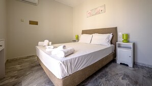 A neatly made bed with white linens and rolled towels, a bedside table with a green lamp, and a wall-mounted air conditioner. - Niriides Villas | Nymfe | Villa 2-bedrooms with private pool (Hersonissos)