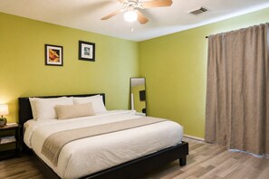 A hotel room with a bed, a nightstand, a lamp, a ceiling fan, and a window with curtains.