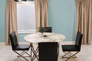 A dining area with a round table, black cushioned chairs, and a vase with green foliage.