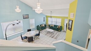 Een eetgedeelte met een ronde tafel en stoelen, een groene zithoek en een kroonluchter.