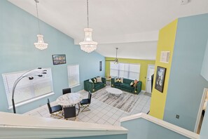 Een eetgedeelte met een ronde tafel en stoelen, een groene zithoek en een kroonluchter.